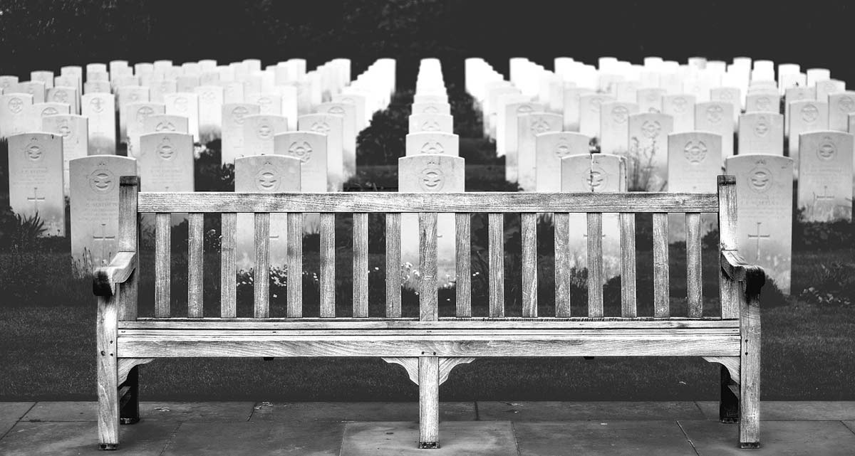 Black and white photo of a traditional cemetery plaques with bench.